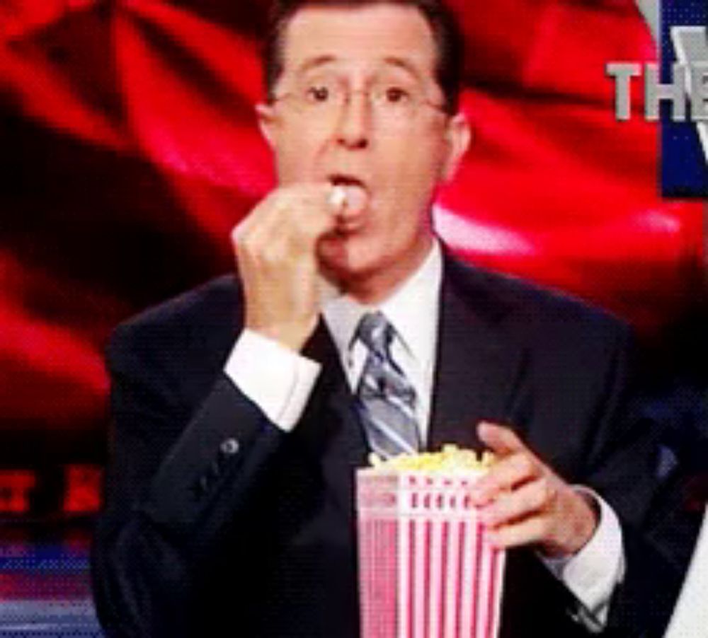 a man in a suit and tie is eating popcorn from a red and white striped container