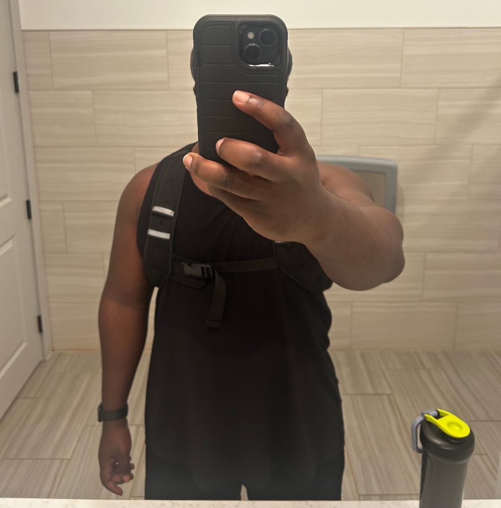 Me, in a black tank and weighted vest, taking a post gym mirror selfie. My phone is held up to obscure my face. 