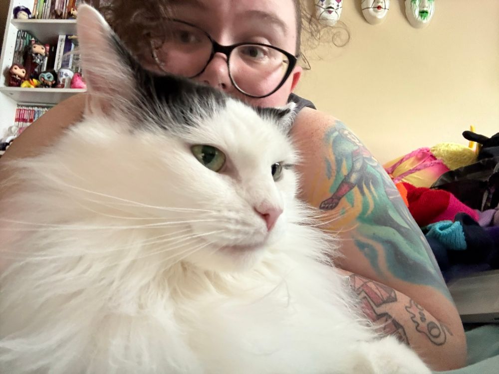 A girl with glasses snuggling a fluffy white and black cat