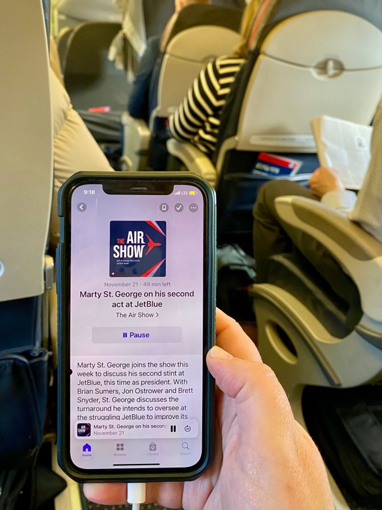 An iphone showing a podcast being played inside an airplane