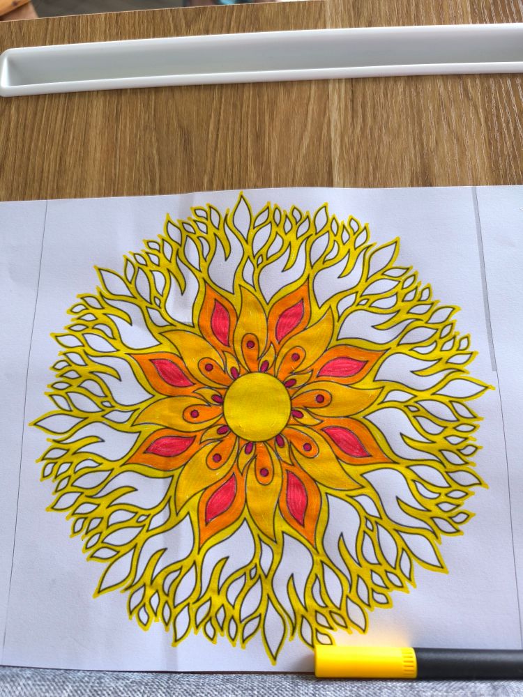 Eine gemalte Blume oder Sonne. In der Mitte ein leuchtend gelben Kreis, dann Blätter oder Sonnenstrahlen in gelb, orange und rot