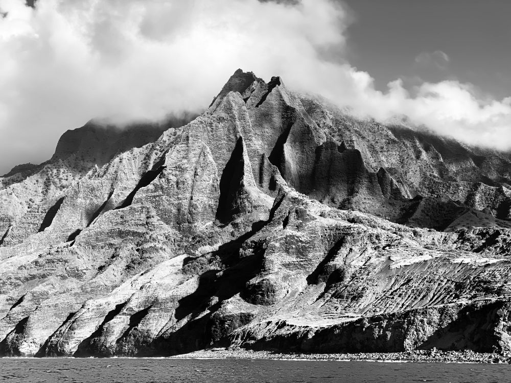 Photo of brown and green jagged mountains on the Napali Coast of Kauai, under a cover of clouds
