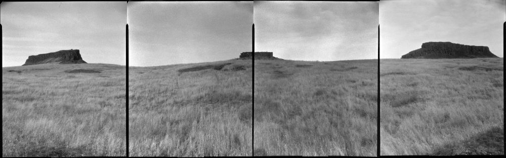 Four panel panorama with two large rock formations on either side, and one in the middle. Grasses make up the foreground. The sky is cloudy. 