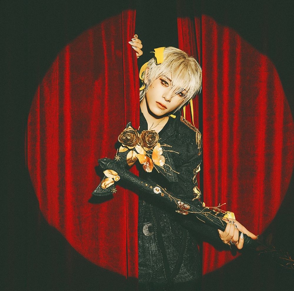 Haru in between a red curtain, holding out his axe. 