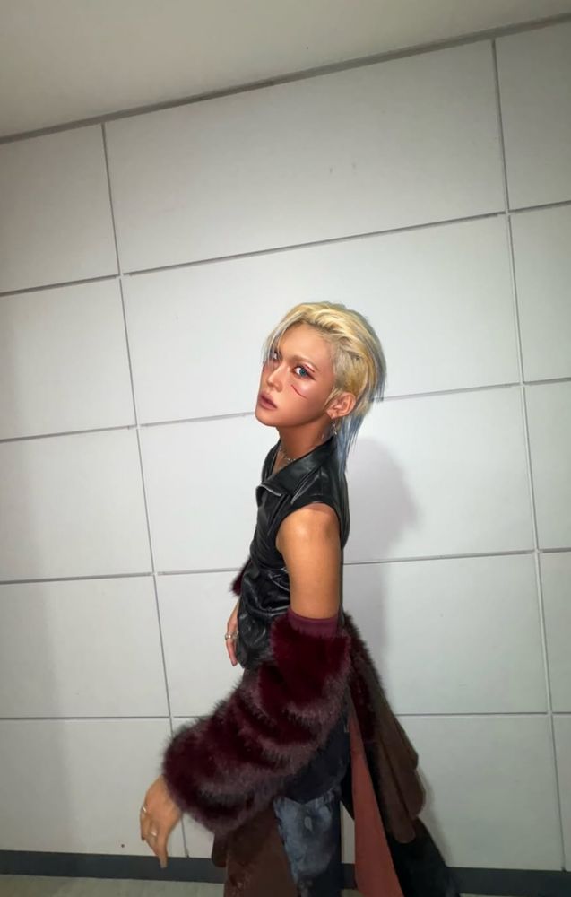 Hyun of xlov in a black leather vest, pants with a brown skirt, and brown fur sleeves. 