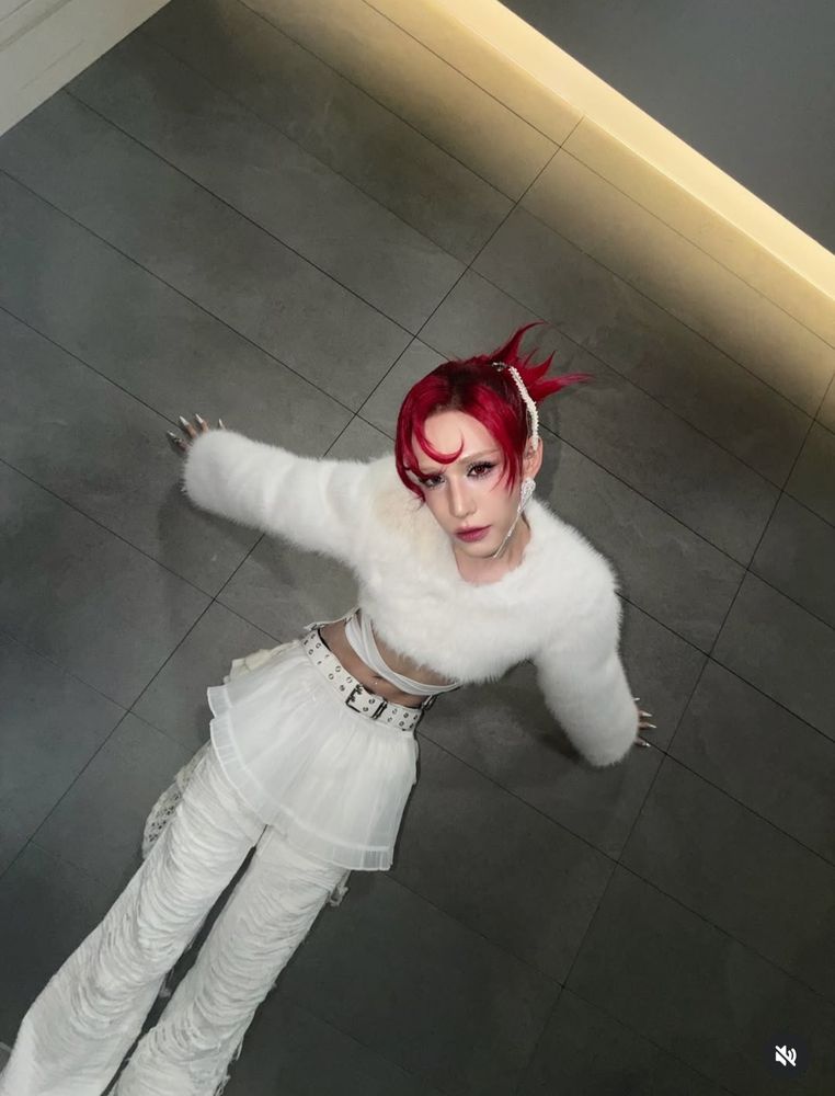 Wumuti of xlov in all white, fur top, pants and skirt, sitting on the ground. 