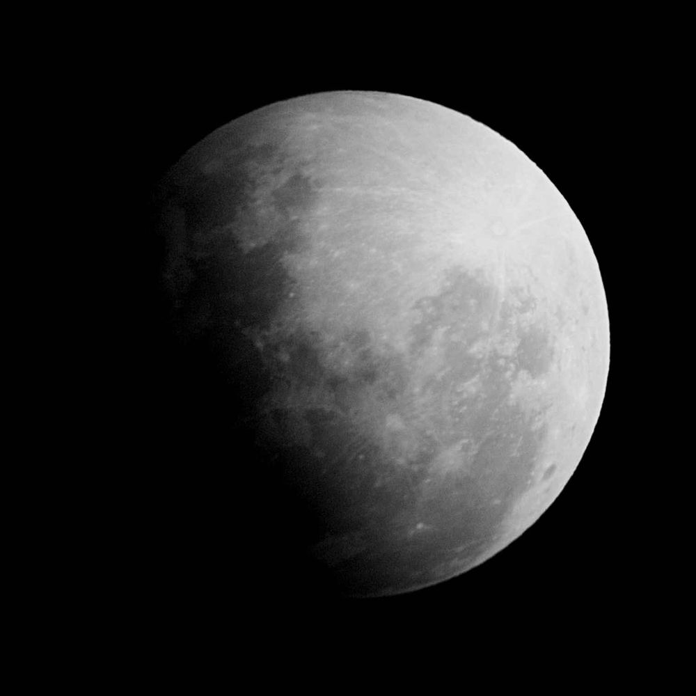 A photo of the moon during a partial lunar eclipse. The earth's shadow casts a dramatic gradient from light to dark across the lunar surface.
