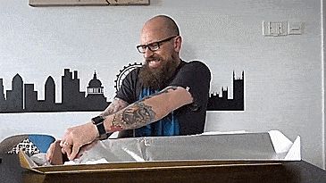 A bald man with an impressive beard struggling to separate a piece of a very large toblerone bar.