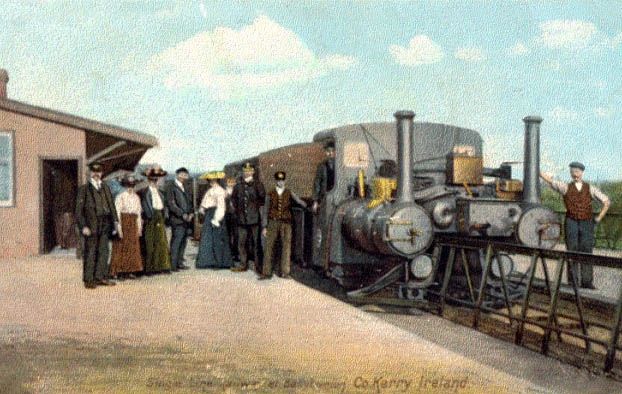 Hand tinted image of the Ballybunion and Listowel Railway, with a steam engine missing it's entire middle section perched on a v-shaped monorail. 