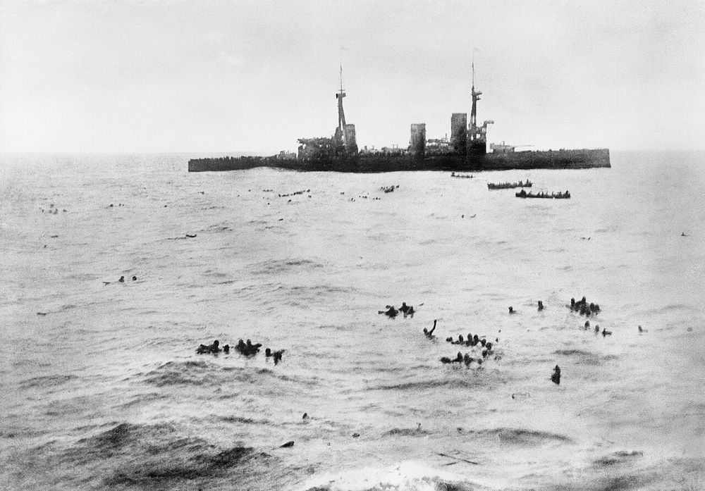 HMS Inflexible picking up German survivors in the aftermath of the battle. The warship sits in the distance as small boats pick up the drifting survivors.