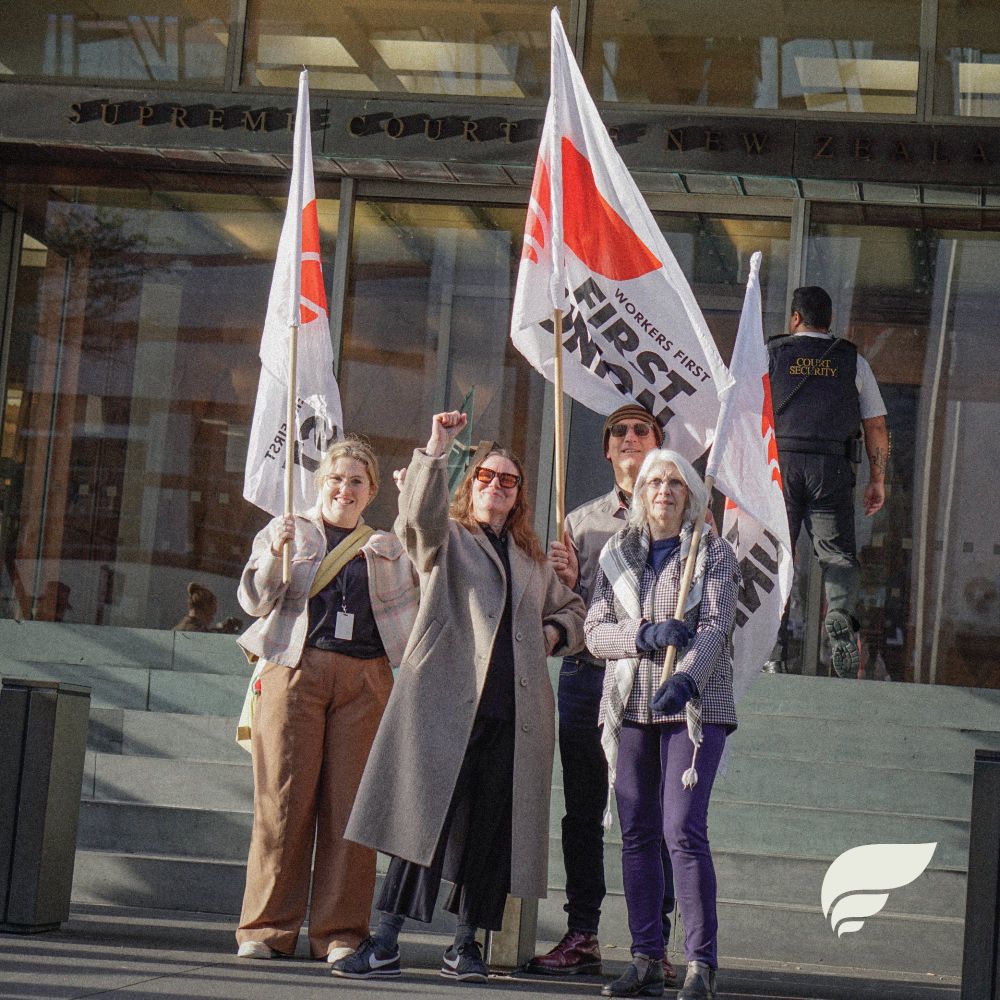 a photo of four people standing on the steps of the new zealand supreme court. three are holding workers first union flags, while the person in the middle has a hand on their hips and is raising a fist skyward. they all look awesome