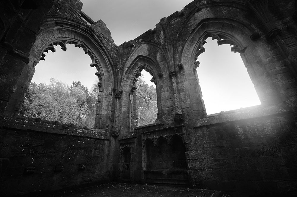 Atmospheric black and white photo of three medieval arched windows in a ruined abbey.