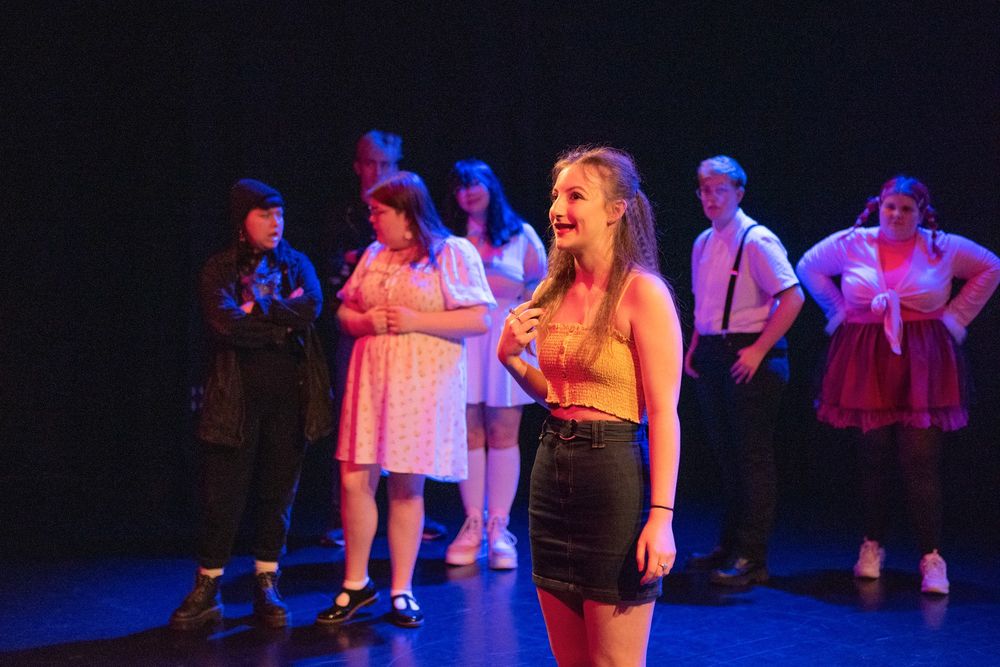 A group of young people on a dark theatre stage with black backdrop