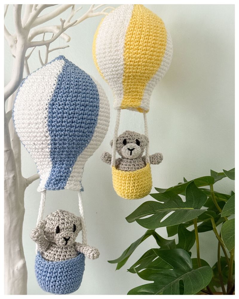  Two Crochet hot air balloons made from a cotton yarn - one is blue and white the other is yellow and white. Each balloon has a small crochet bear sitting in its basket. Part of the Up, Up and Away collection by From My Hook, featuring the refreshed bear pattern with new photos and customisation guide.