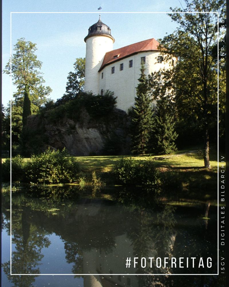 Ansicht des Gebäudes auf dem Burgfelsen von einem Gewässer des Rabensteiner Dorfbachs. Der runde Turm neben der weißen Fassade mit ziegelgedecktem Dach ist mit einer Kappe bekrönt.