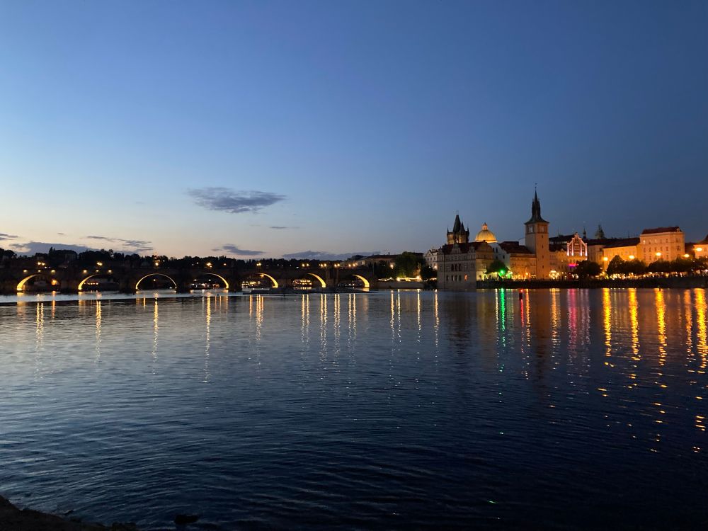 Charles bridge in Prague at dawn, lights reflecting in the water 