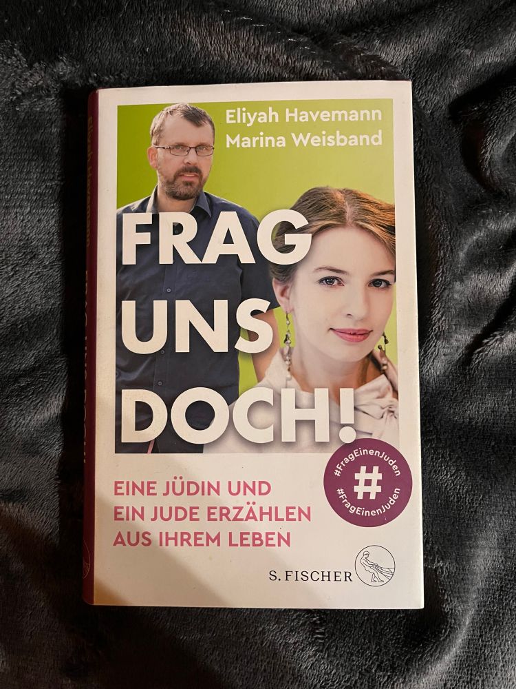 Auf dem Bild ist das Buchcover von „Frag uns doch!“ von Eliyah Havemann und Marina Weisband zu sehen.
Das Cover zeigt die Porträts der beiden Autor*innen vor einem grünen Hintergrund.
Darunter steht der Untertitel: „Eine Jüdin und ein Jude erzählen aus ihrem Leben“.
Rechts unten befindet sich ein lilafarbener Kreis mit den Hashtags #FragEinenJuden und #FragEinenJuden.
Das Buch ist im Verlag S. Fischer erschienen.