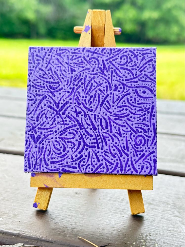 Purpura (Latin for purple) 3 inches by 3 inches canvas on a mini easel

Purpura is a light purple background with various lines, shapes, dots, and symbols covering the entire canvas and sides in a darker purple