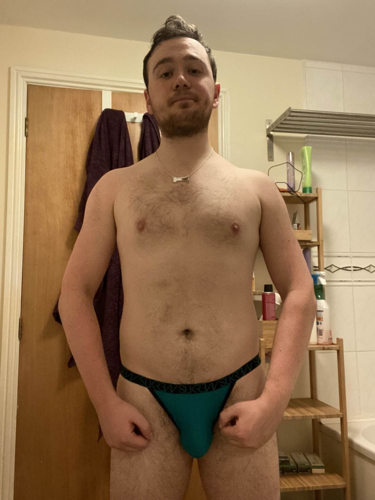 John a white male - is posing in the bathroom in a green thong while wearing a reflective bone shaped necklace 