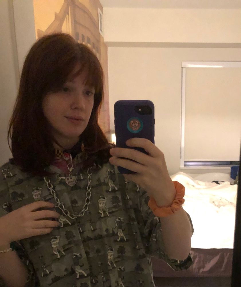 He/they dog boy with maryland collar and chain collar in a hotel room with an oversized st bernards golfing shirt. He looks tired and soft and is smiling faintly.