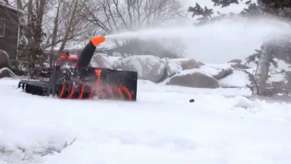 a snow plow is blowing snow in a snowy yard .