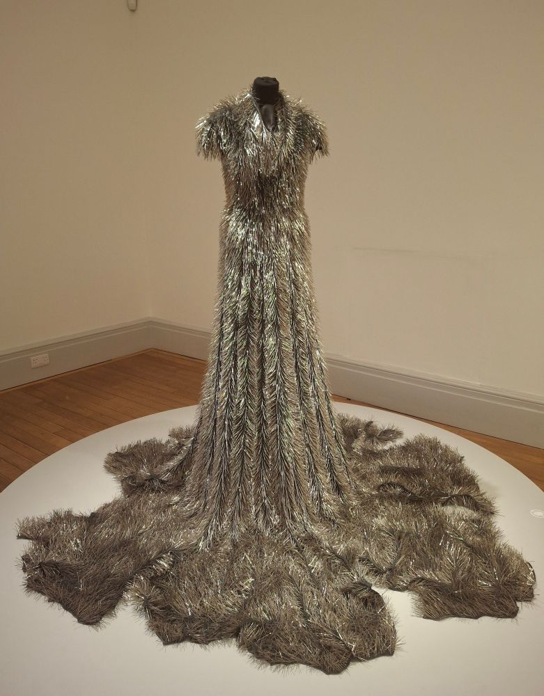 A floor length, mermaid tail dress thickly covered with dressmakers pin so the whole dress is silver and spikey