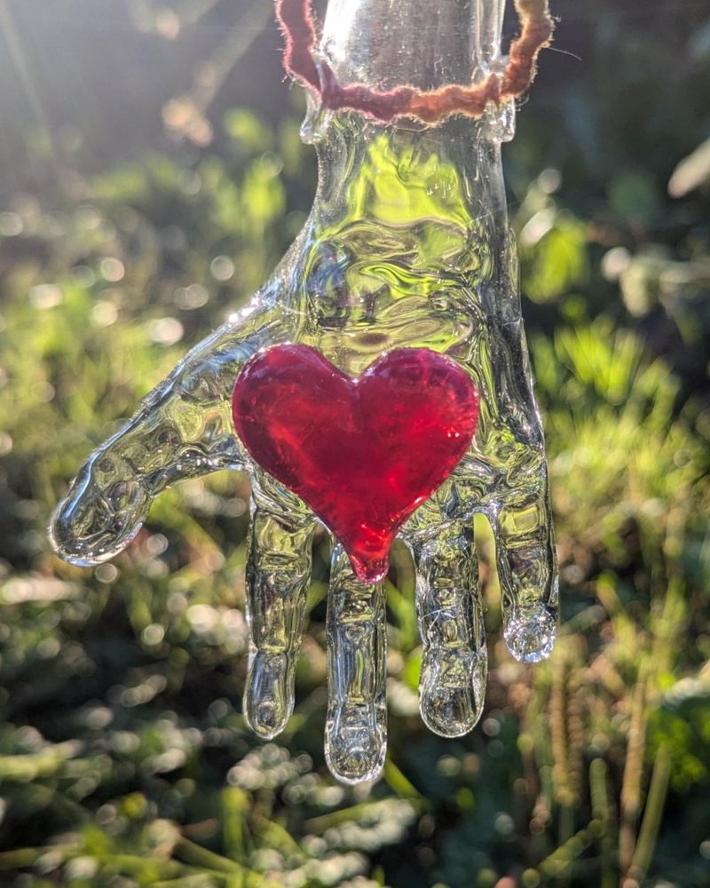 A clear glass hand with a pink heart in its palm. 