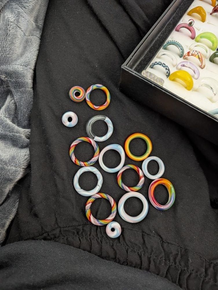 Queer and Trans Pride glass rings. Colorful glass circles of various patterns on a black background. 