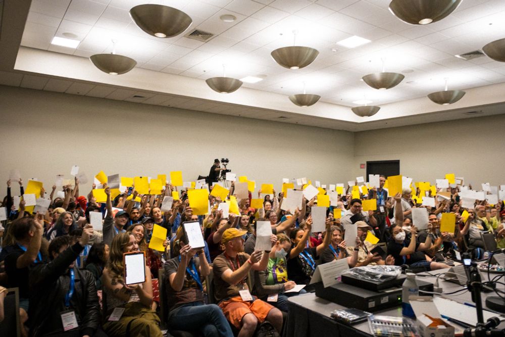 A photo of a room full of people at San Diego comic-con 2025 all holding up drawings of their octopuses. 