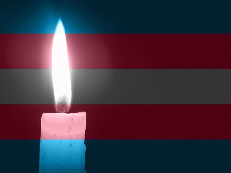 A transgender flag with a glowing candle in front of it 