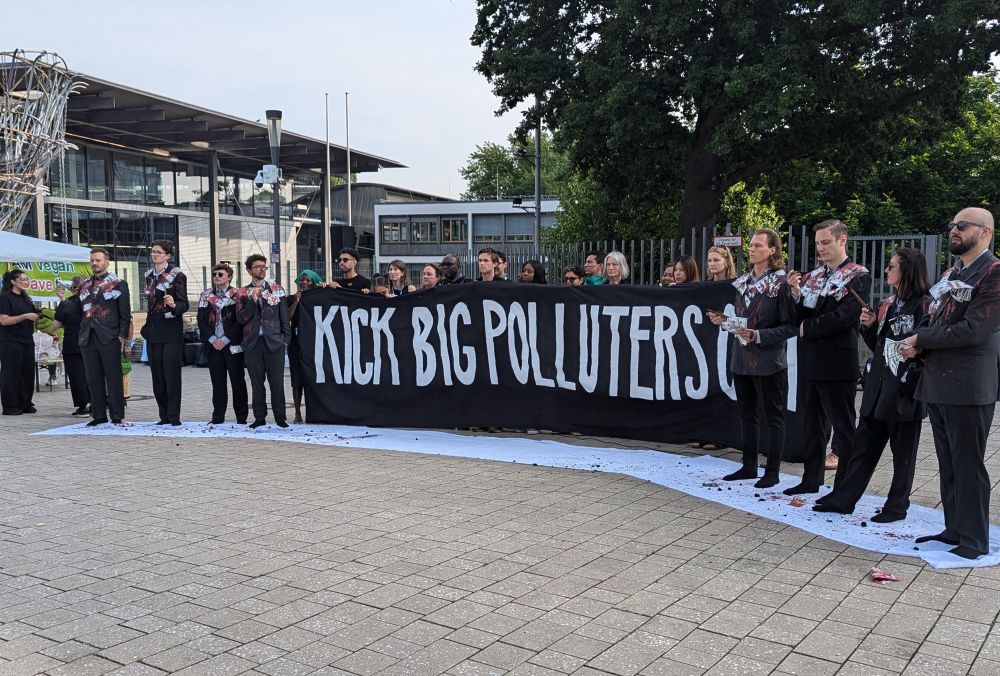 Banner "Kick big polluters Out" und Menschen im Anzug, die mit Geld behängt sind. 