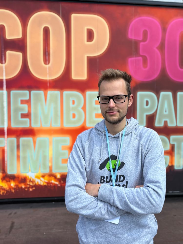 Robert mit verschränkten Armen vor einem COP30 Plakat