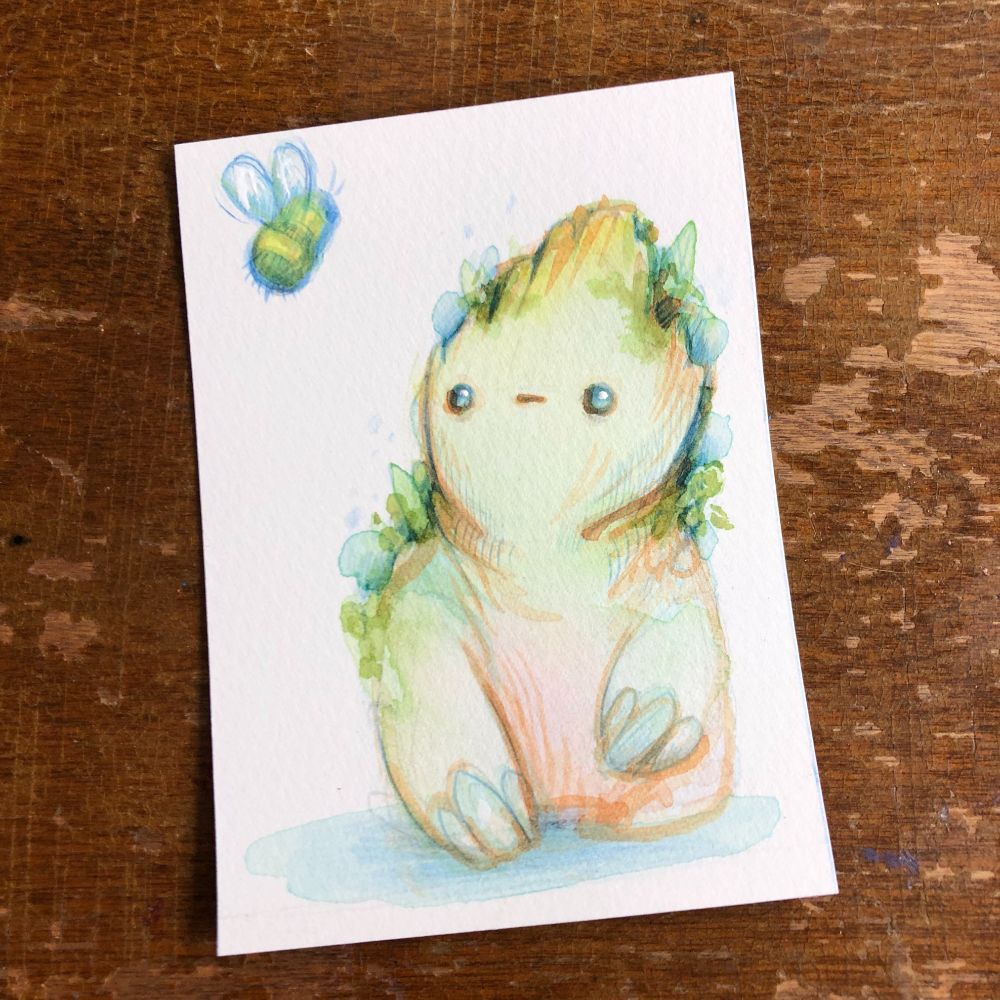 A cute watercolor painting resting on a wooden table. The painting is a sort of stumpy tree spirit with beady black eyes staring at a bumblebee. 