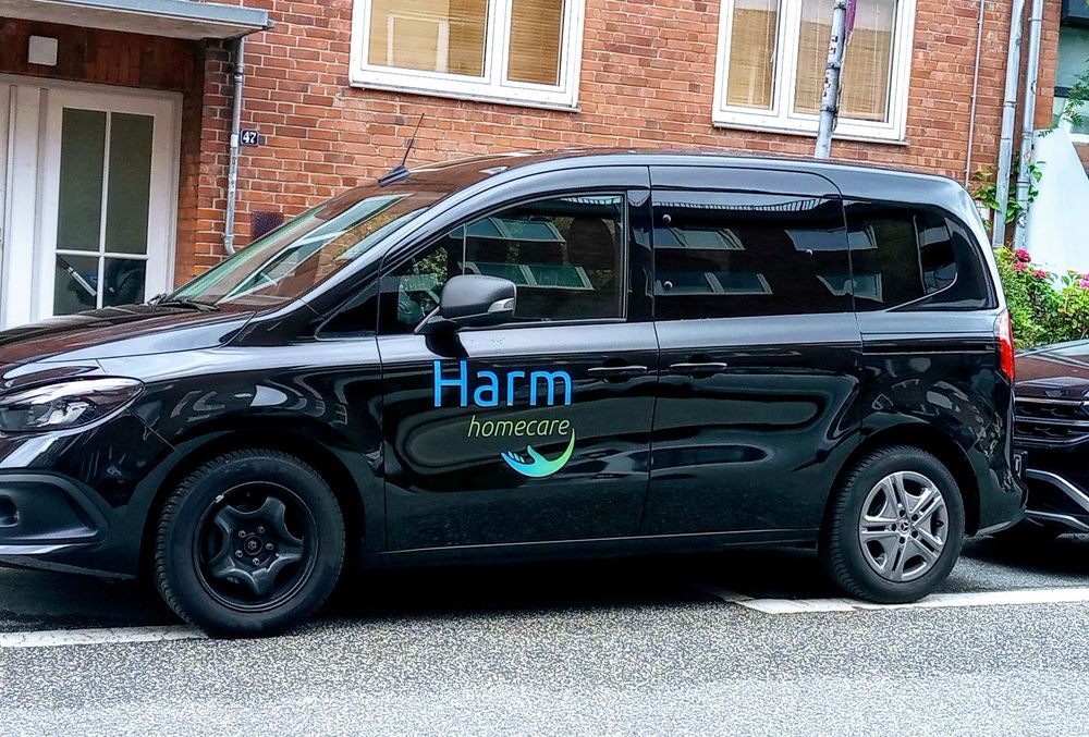 A car parked on the site of a street. On the side of the car, there's a company logo that says: "Harm homecare"