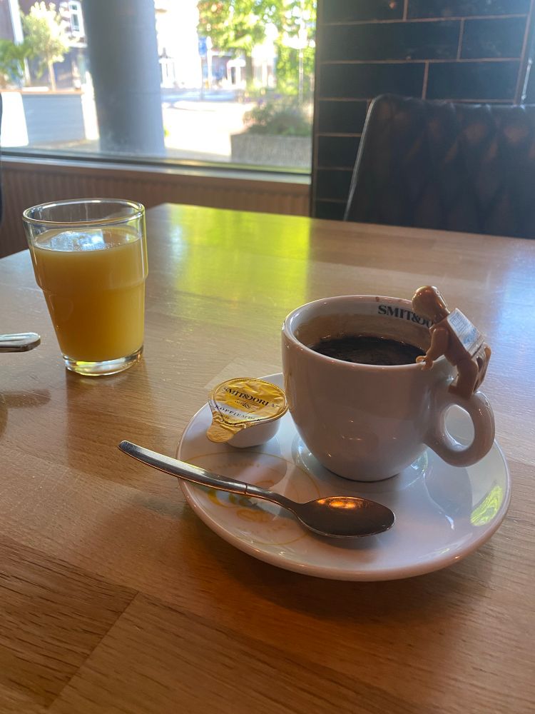 Tisch mit Orangensaft und gefüllter Espressotasse. Auf dem Henkel steht die Legofigur C3PO und schaut in die Tasse.