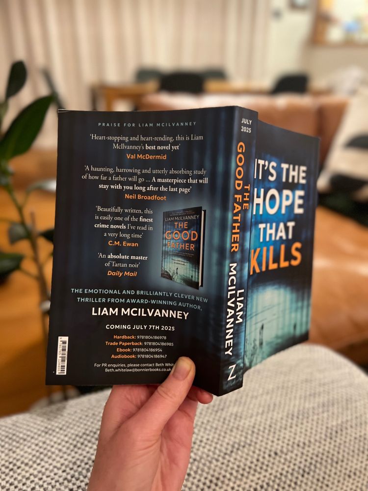 Hand holding up a copy of The Good Father by Liam McIlvanney against background of living room