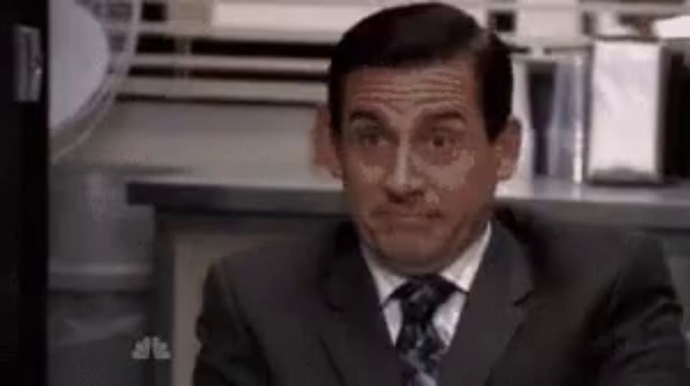 a man in a suit and tie is sitting at a desk and making a funny face .