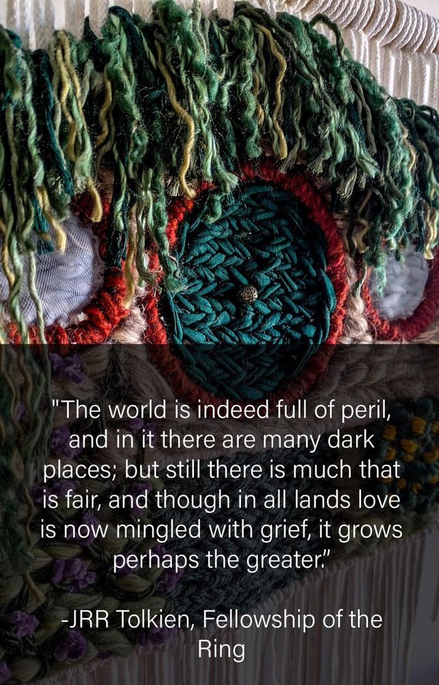 A tapestry featuring a Hobbit home inspired by the Lord of the Rings, Fellowship of the Rings novel. The tapestry features fibers such as yarn and string in the shape of a home with a round door built into a hillside and with various colors and shades of green yarn hanging over the roof. The photo has an text box that reads "The world is indeed full of peril, and in it there are many dark places; but still there is much that is fair, and though in all lands love is now mingled with grief, it grows perhaps the greater." JRR Tolkien, Fellowship of the Ring