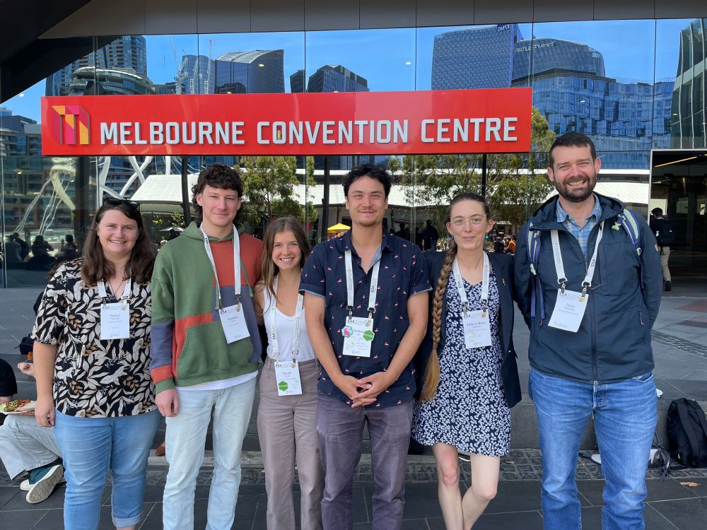 Sonya, Sam, Nicole, Josh, Hilary Rose, and Sean smile for a group photo in front of the Melbourne Convention Centre. 