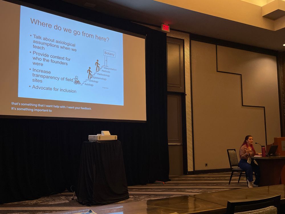 A slide for Where do we go from here? Including talk about axiological assumptions, provide context for who the founders were, increase field site transparency, and advocate for inclusion. Haley is presenting sitting to the side. 