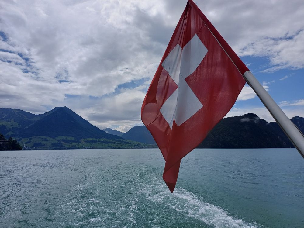 A mountain scene in the background, in the foreground the lake with the flag of Switzerland. 