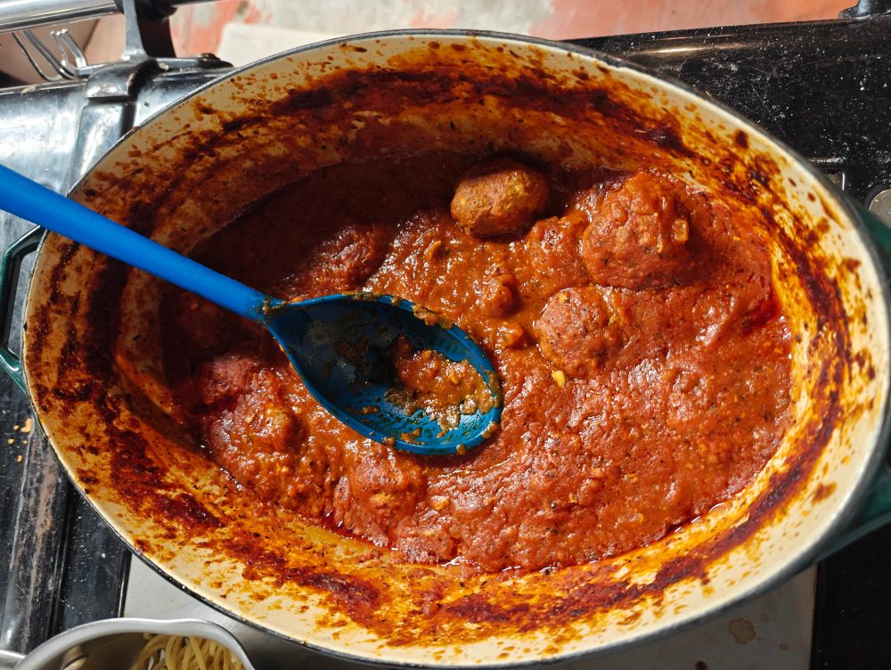 Pot on stove containing spaghetti sauce with ground pork gluten-free meatballs, a blue silicone spoon in the pot. The recipe is as follows:

Two pounds lean minced meat, such as beef or pork
One half cup breadcrumbs, gluten-free work fine
Two eggs, beaten
One quarter cup finely chopped onion
Two cloves garlic, crushed or finely chopped
Salt and pepper to taste, optional

Combine ground meat, eggs, onion, and garlic, mixing thoroughly, Shape meat mixture into twenty-four two-inch meatballs. Bake meatballs on a rack on broiler pan, or on a parchment-lined baking sheet for thirty minutes at 350 degrees Fahrenheit. Meatballs can then be added to two jars of red sauce and cooked for an hour or until time of your choosing. Or eat meatballs sans sauce. Enjoy!
