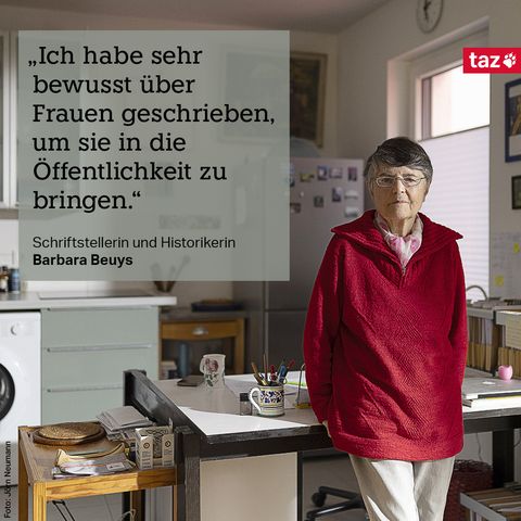 Barbara Beuys in ihrer Wohnküche. Sie lehnt am Schreibtisch, dahinter eine Küchenzeile. Text: „Ich habe sehr bewusst über Frauen geschrieben, um sie in die Öffentlichkeit zu bringen.“ Schriftstellerin und Historikerin Barbara Beuys 