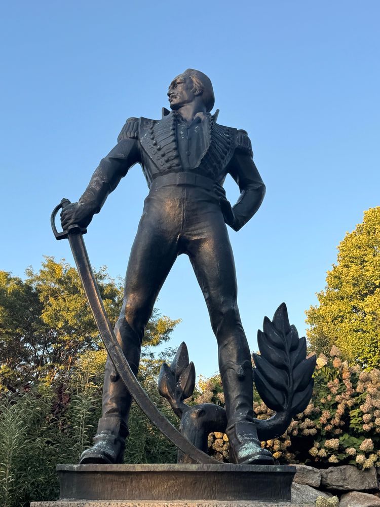 An 18th century statue of a man with a cutlass in a waistcoat, standing dramatically with a hand on his hip and his head turned to the side 