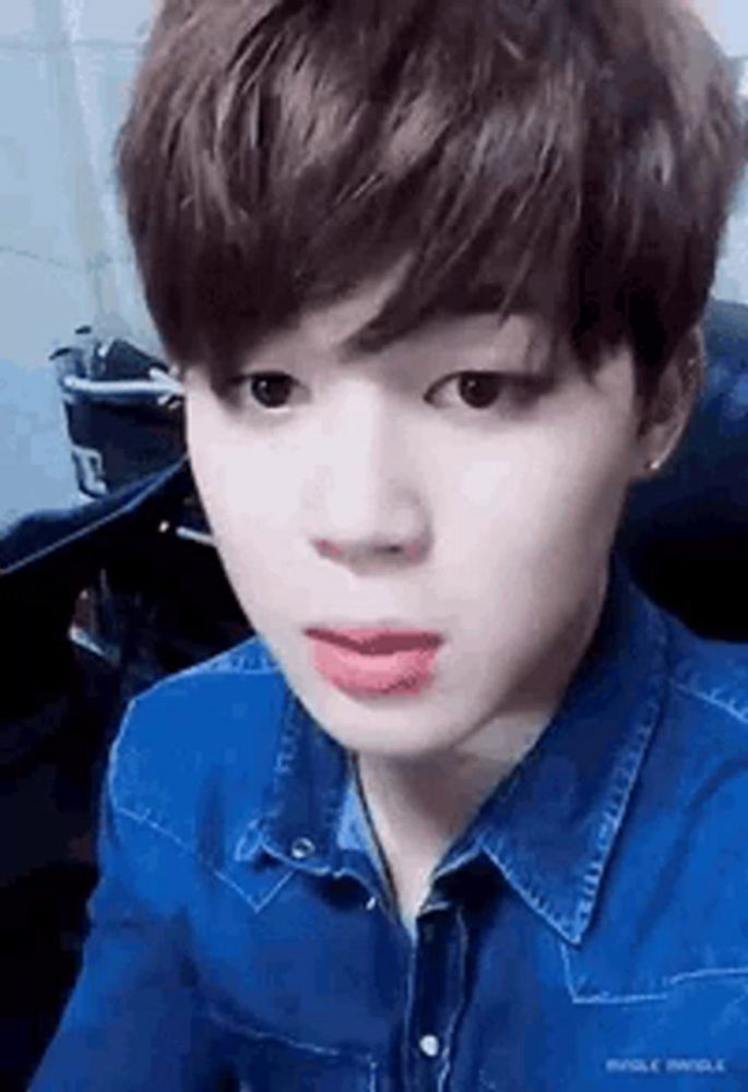 a close up of a young man wearing a blue denim shirt with his mouth open .