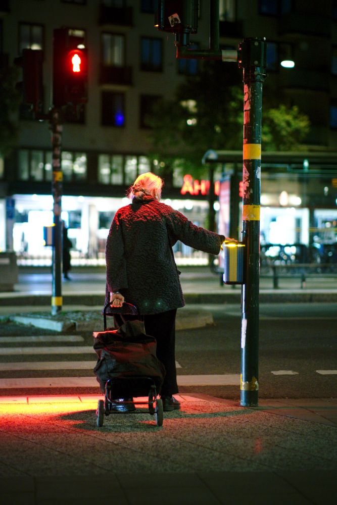 A person waiting to cross the street at a red traffic light in the dark, red light on her shoulders and head. 