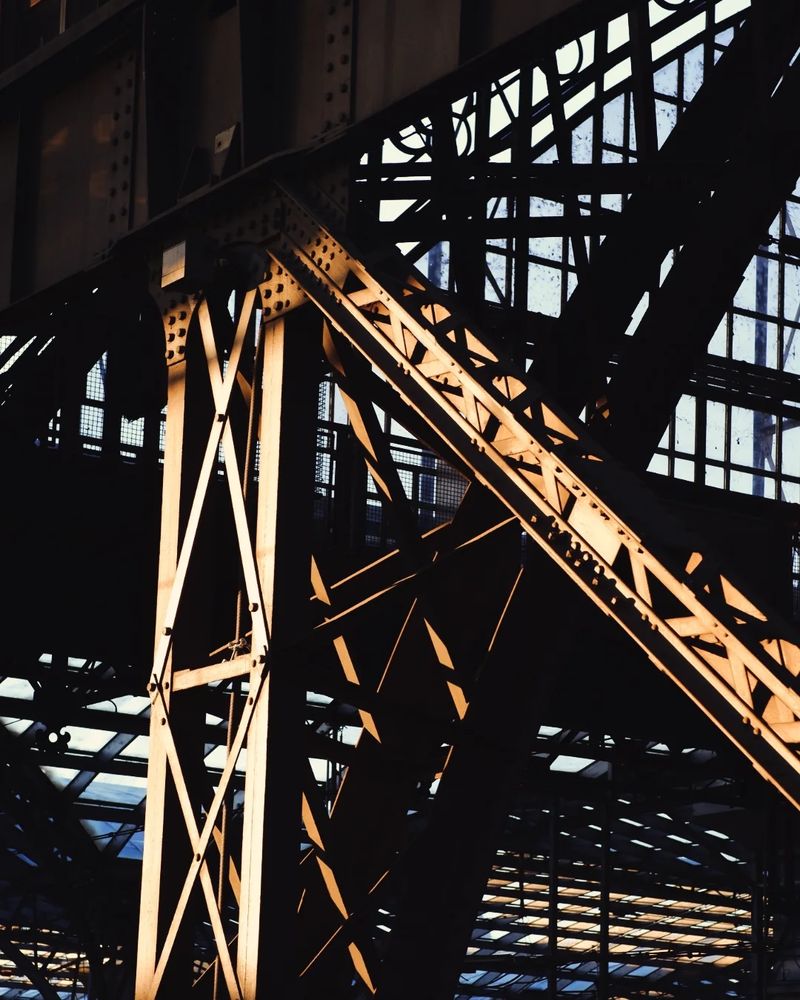 Golden light on steel beams in a train station hall, the afternoon sky is visible through window fronts in the background. 