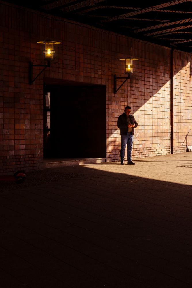 Man standing in a triangle of sunlight cast under a railway bridge.