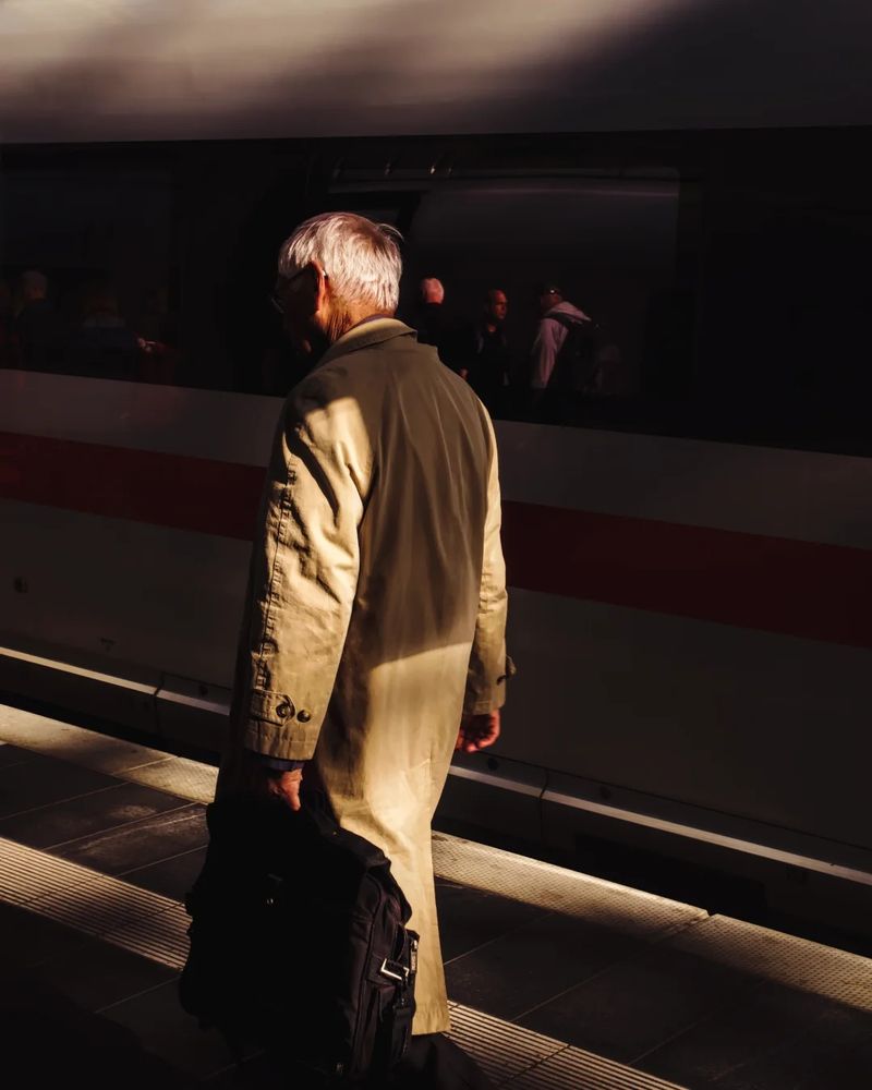 Man walking along a train, golden evening light partly illuminates him while the train remains in the shadow. 