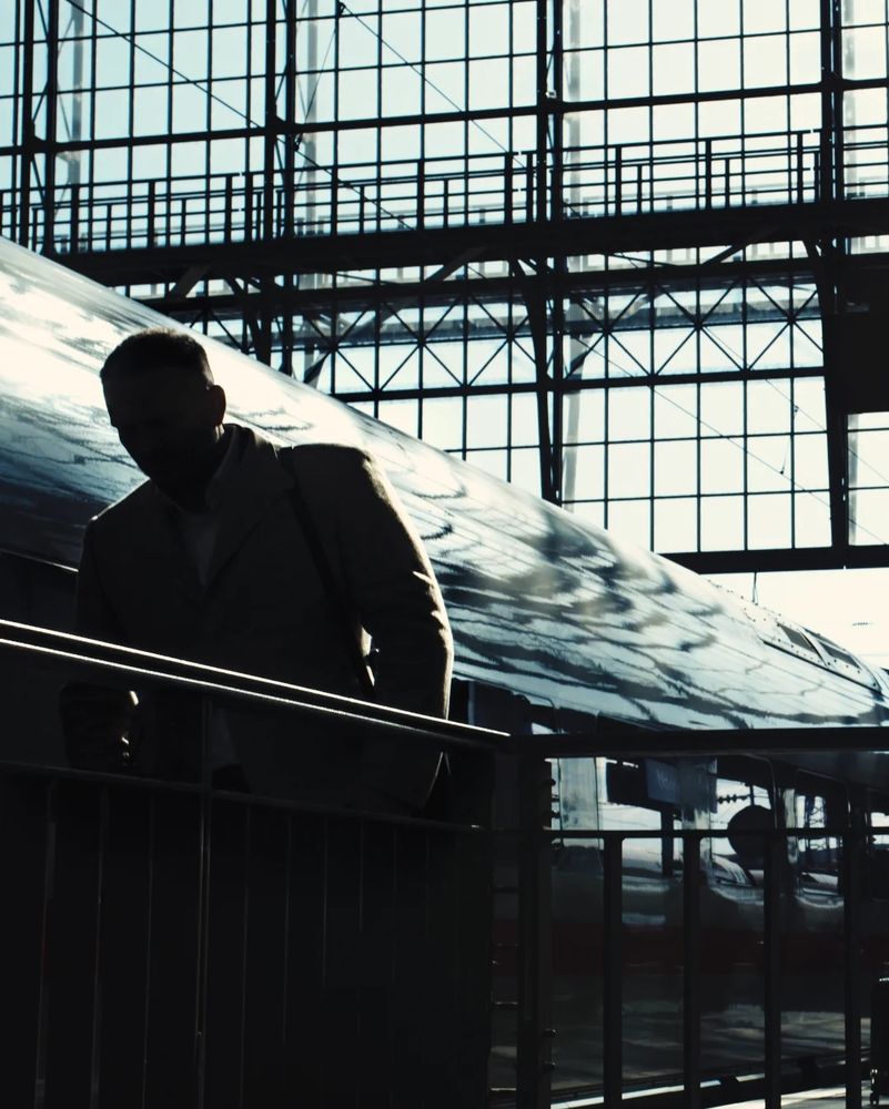 Silhouette shot of a man in front of a shiny white train, backlit by the afternoon sky on the background. 